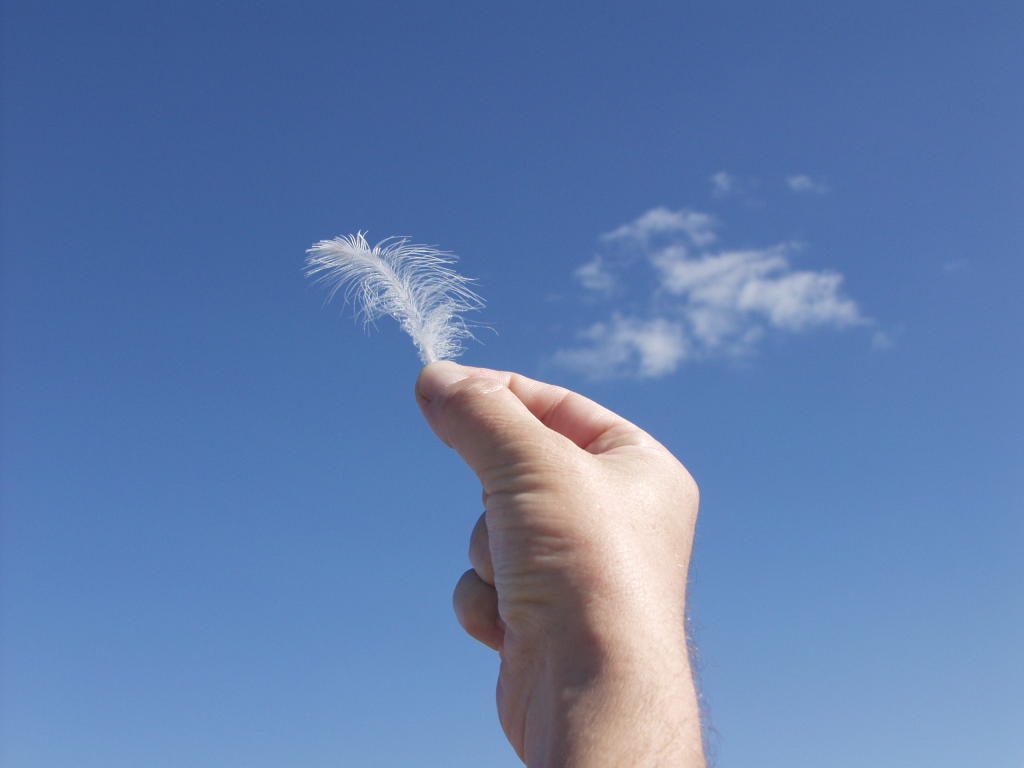 Hand mit Feder vor blauem Himmel